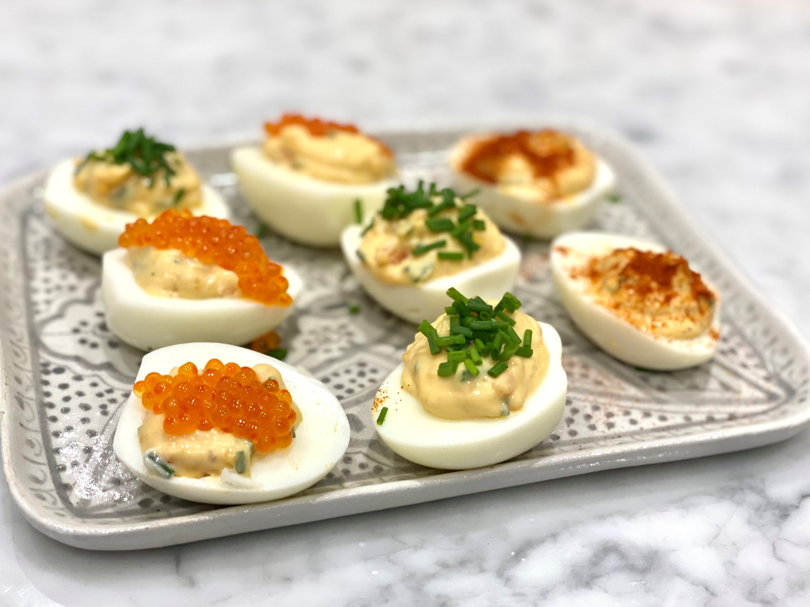 Deviled Eggs. A silver tray with halved eggs topped with a salad filling and trout roe, and herbs sprinkled on top. The best anti-inflammatory snack.