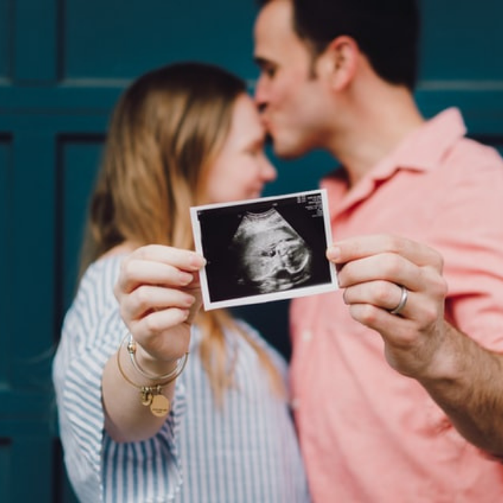 A man kissing a female's head as they hold a baby scan picture.