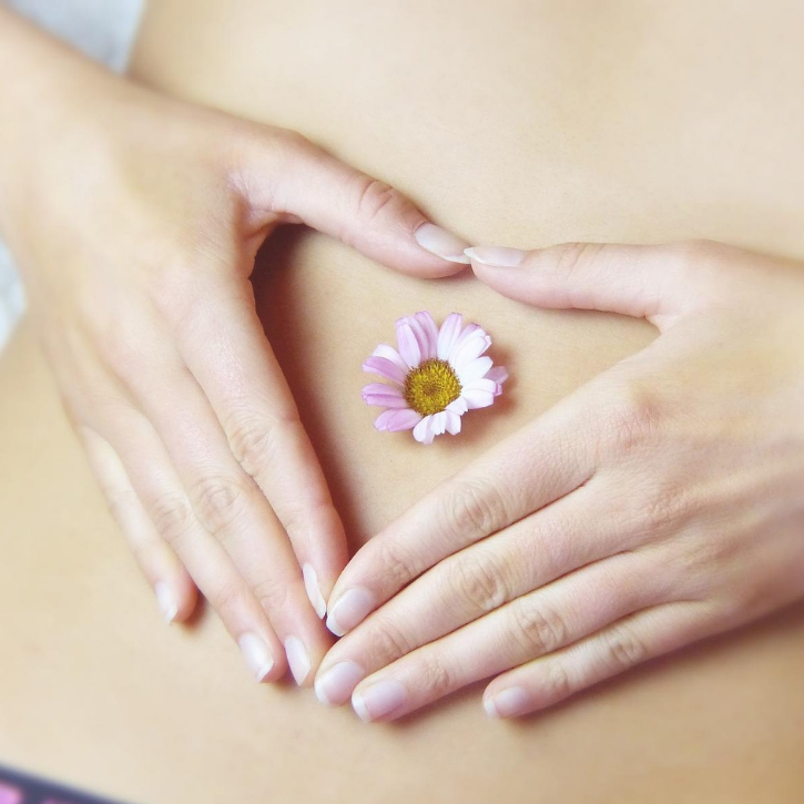 A female stomach making a heart with her hands and a flower on her tummy button.