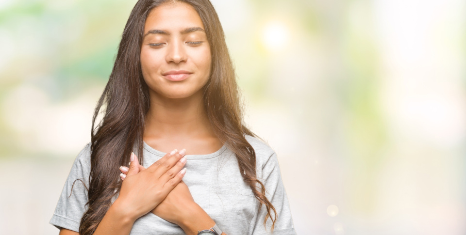 Female, closed eyes, holding her hands on her heart, smiling, indicating gratitude.