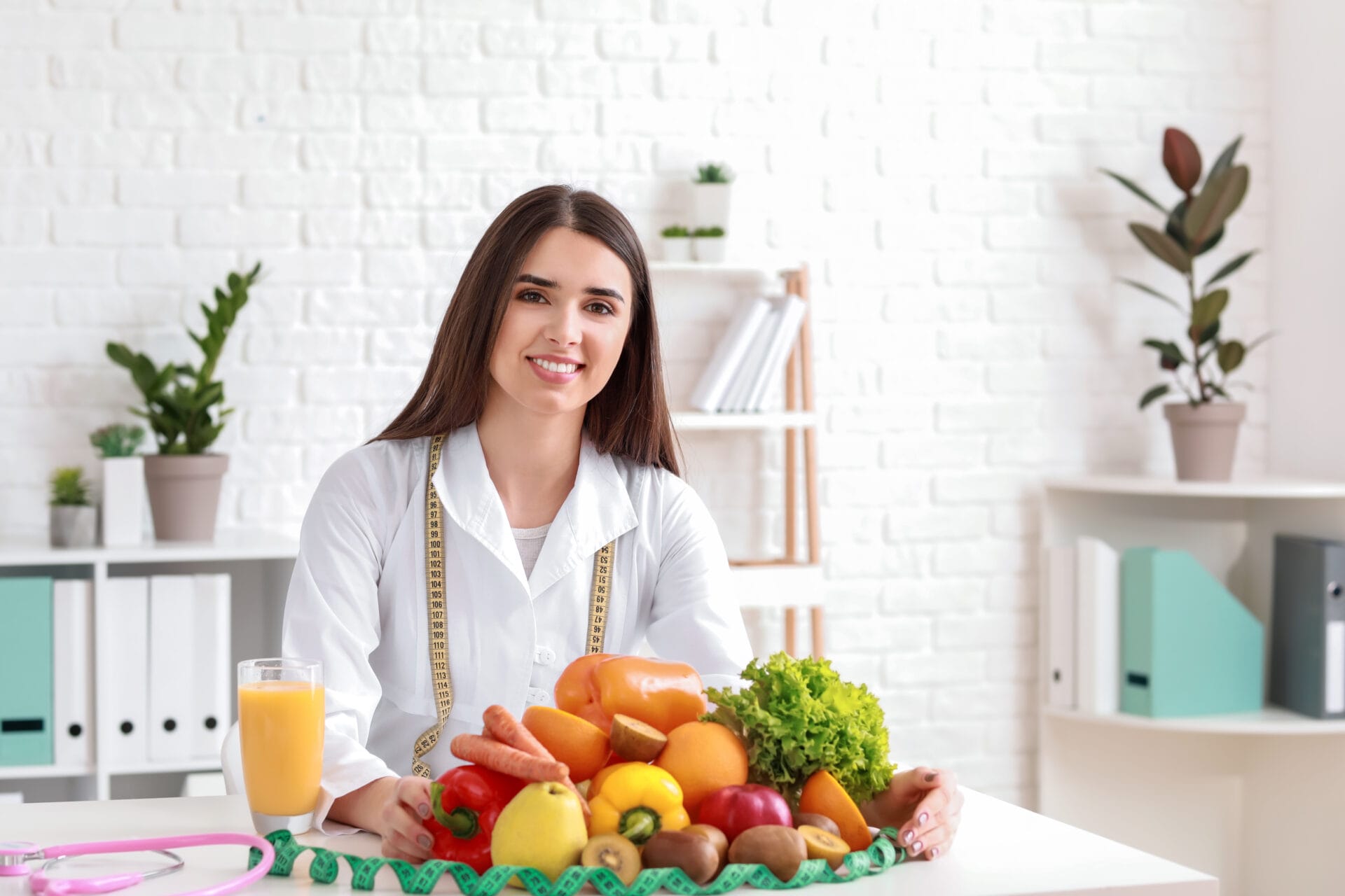Nutritionist for immune health, in front of a bowl of fruit and vegetables, with a measuring tape.